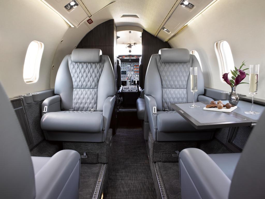 Completed business aircraft cabin with gray leather seating, diamond quilting, fitted carpet, and dark cabinetry.