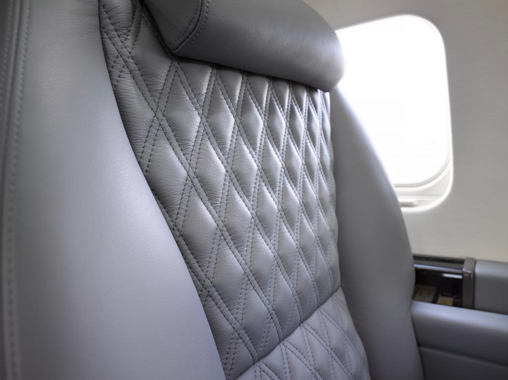 Close view of gray leather aircraft seat upholstery with aligned diamond stitching and a shaped headrest.