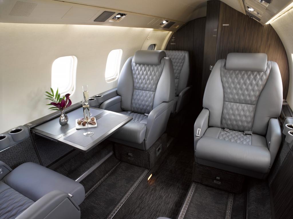 Completed business aircraft interior with gray leather club seating, a cabin table, fitted carpet, and dark cabinetry.